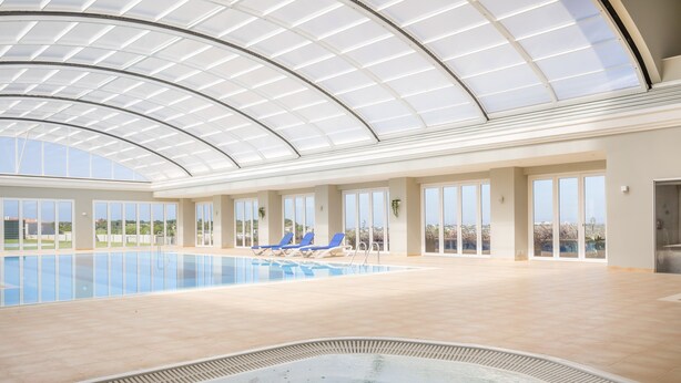 An indoor swimming pool with a glass ceiling, blue lounge chairs, and a hot tub. - Casa Makin at Boa Vista Golf Resort, Bayview Village (Lagos)