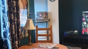 Ein kleiner, gemütlicher Raum mit einem runden Holztisch, einem blauen Stuhl, einer Lampe und einem Bild an der Wand.