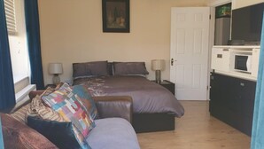 Ein Schlafzimmer mit Bett, Nachttischen, einer Couch, einer Mikrowelle und einer Tür.