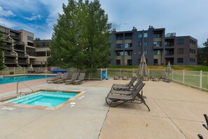 A pool area with lounge chairs and umbrellas, surrounded by apartment buildings.