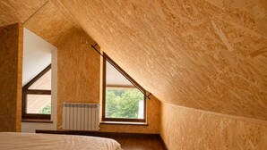 Une chambre avec un plafond en pente, des murs en bois, un lit, un radiateur et une fenêtre donnant sur des arbres.