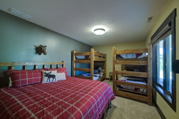 Un dormitorio con una cama individual, dos camas literas, una cabeza de animal montada en la pared y una ventana con persianas.
