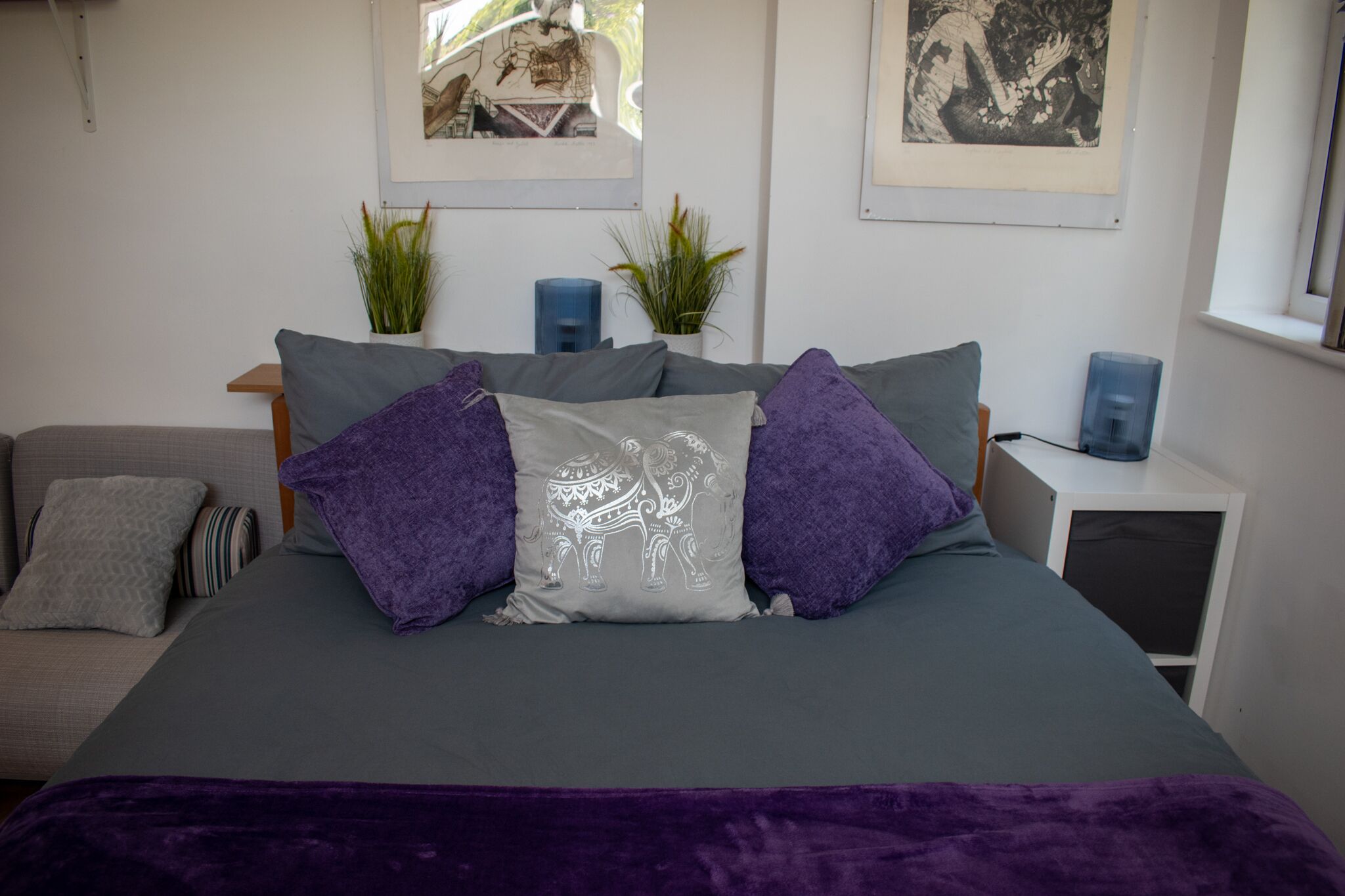 A neatly arranged bedroom with a large bed, two side tables, a small sofa, and two potted plants.