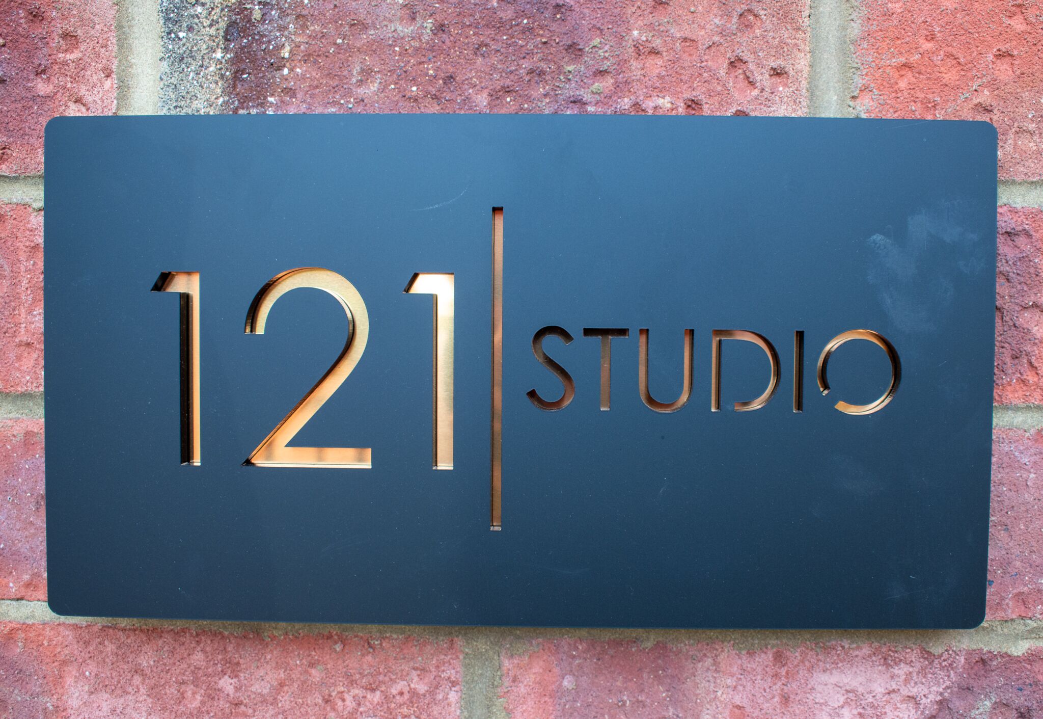 A dark blue sign with the numbers "121" and the word "STUDIO" in gold, mounted on a brick wall.