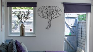 A bedroom with a bed, a window with a view of a garden, and a geometric wall decoration. - 121 Studio (Bishop's Stortford)