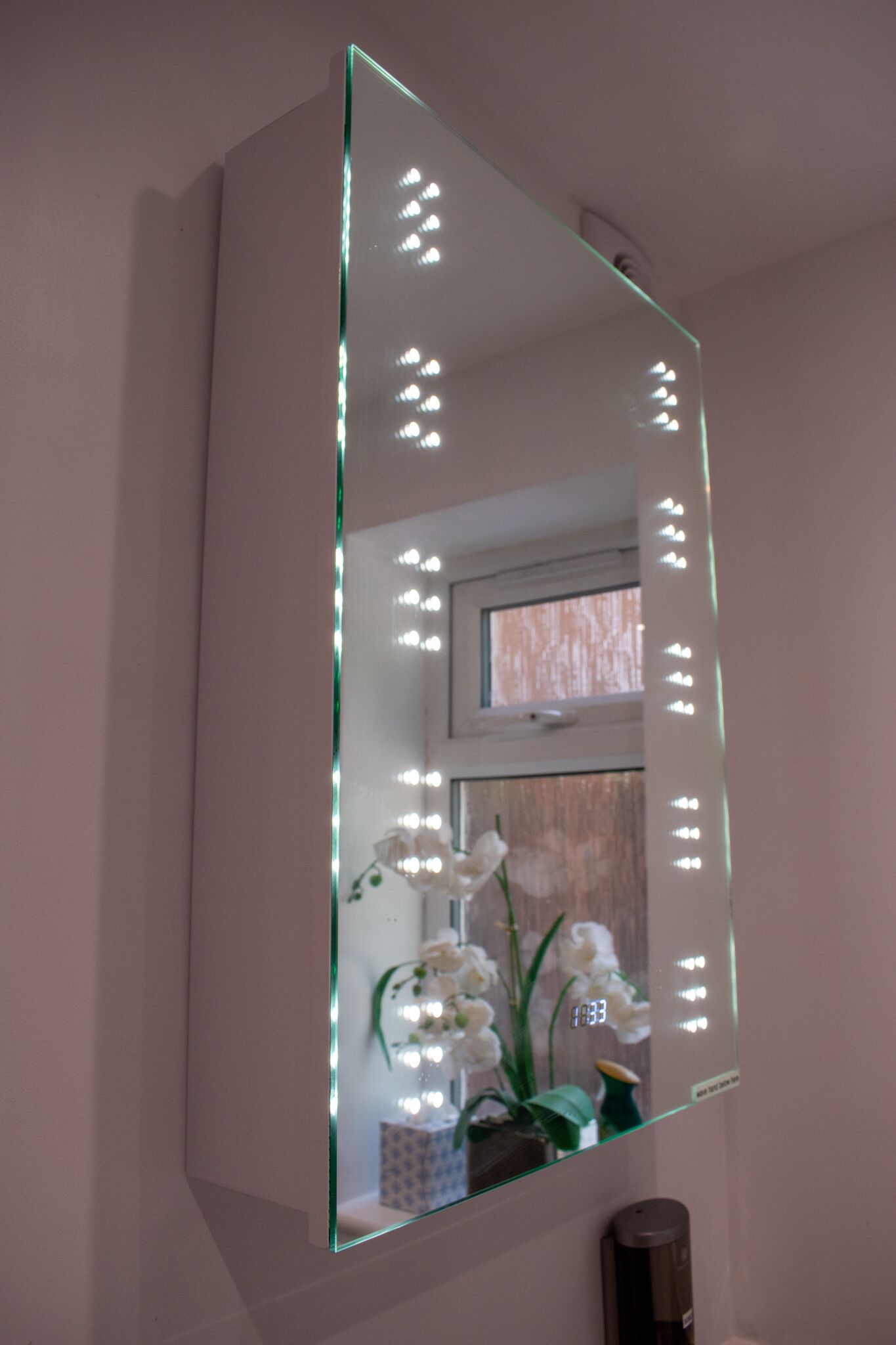 Un baño con un espejo grande, iluminación y una orquídea en maceta.