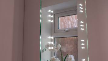 Un baño con un espejo grande, iluminación y una orquídea en maceta.