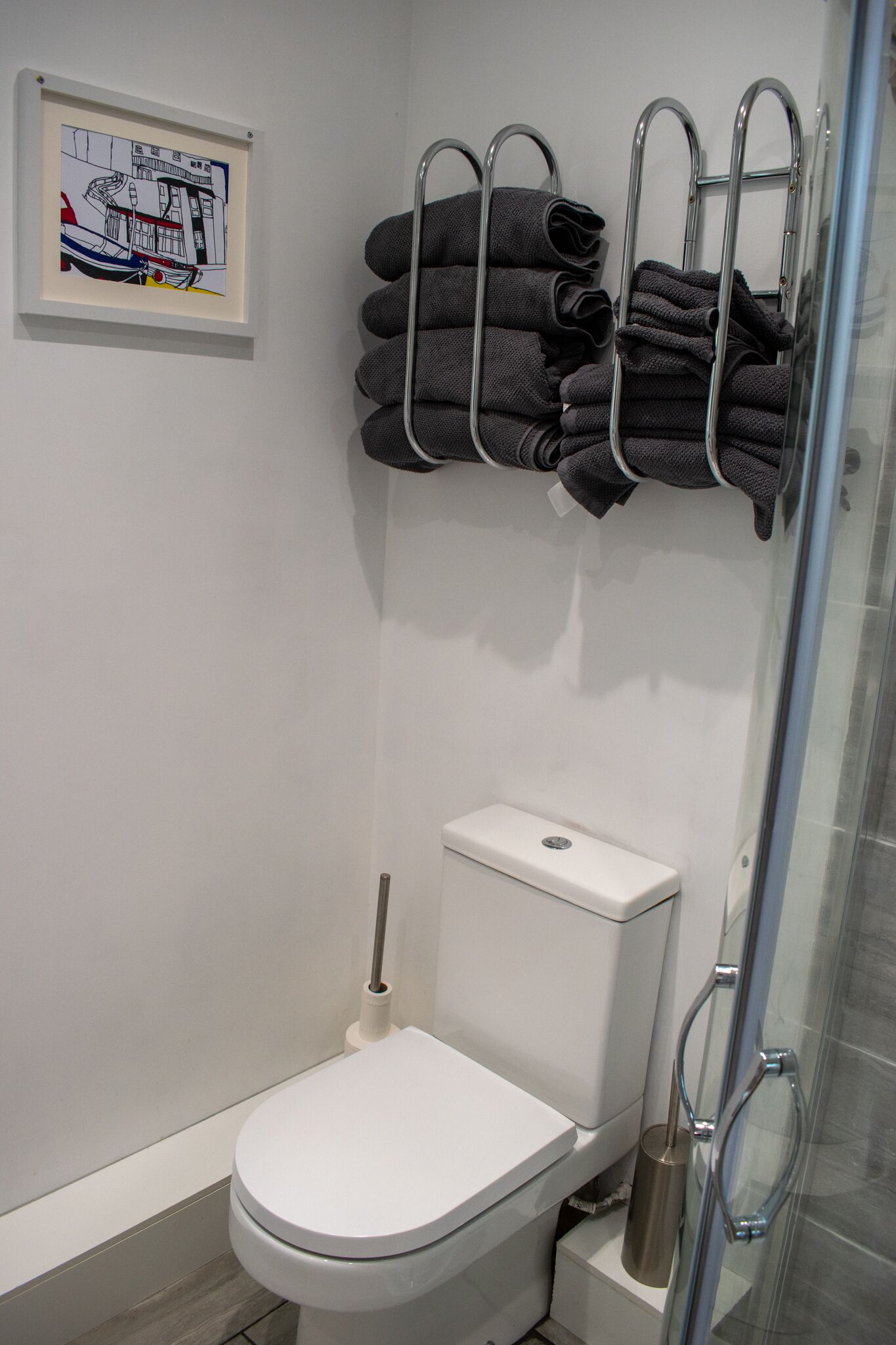 Ein modernes Badezimmer mit einer weißen Toilette, einer Duschkabine aus Glas und einem Handtuchhalter mit mehreren gefalteten Handtüchern.