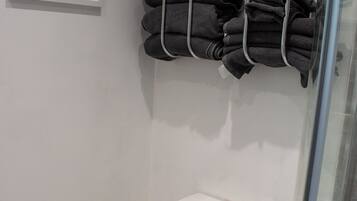 Ein modernes Badezimmer mit einer weißen Toilette, einer Duschkabine aus Glas und einem Handtuchhalter mit mehreren gefalteten Handtüchern.