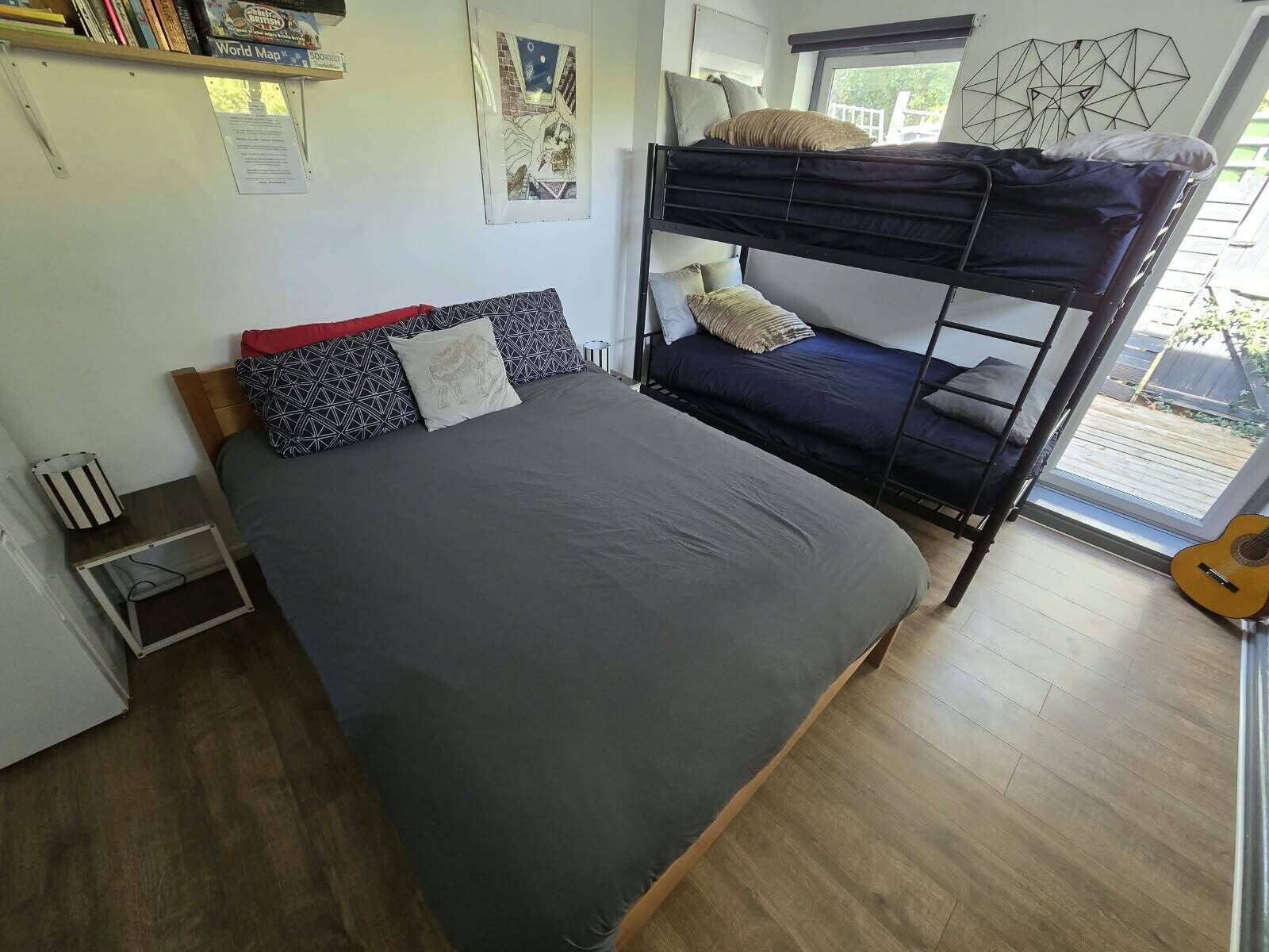 A bunk bed room with a single bed, a small table, a guitar, and a window with a view.