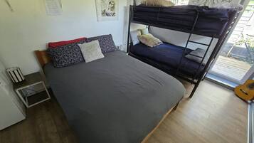 A bunk bed room with a single bed, a small table, a guitar, and a window with a view.