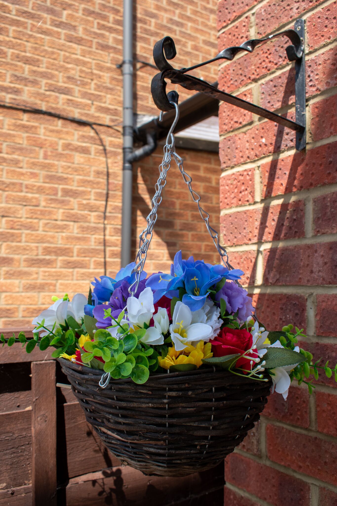 Un cesto appeso con diversi fiori davanti a un muro di mattoni.