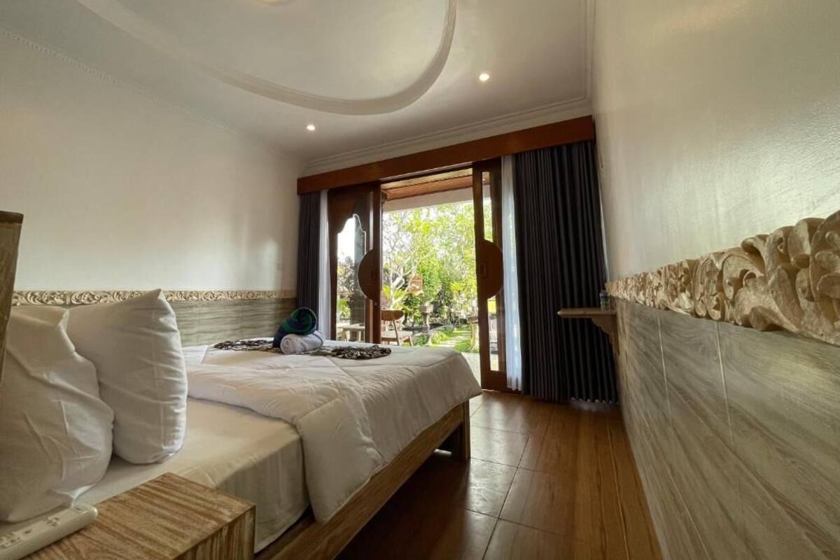 Ein Hotelzimmer mit Bett, Nachttisch, Fenster mit Vorhängen und Blick ins Freie.