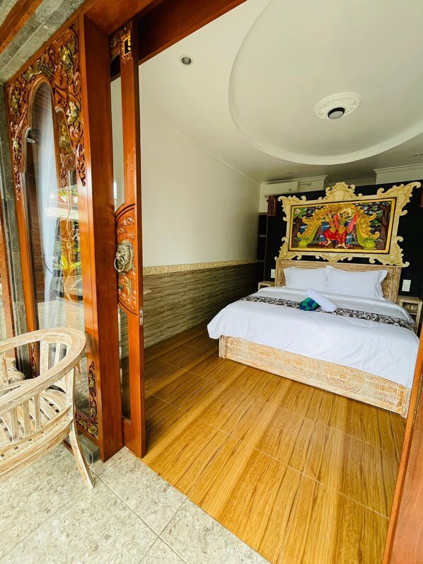 A bedroom with a bed, a chair, and a painting on the wall. - Mikuk Cottages Canggu (Canggu)