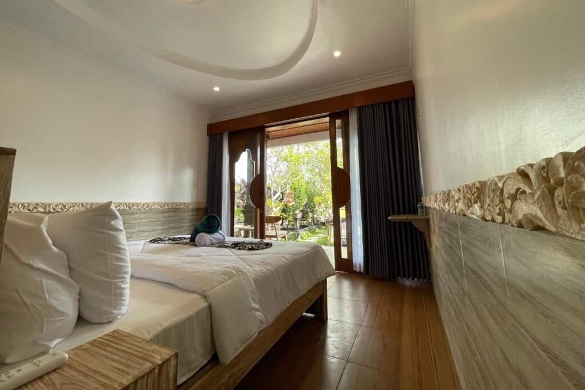 Ein Hotelzimmer mit einem Bett, einem Nachttisch, einem Fenster mit Vorhängen und Blick ins Freie.