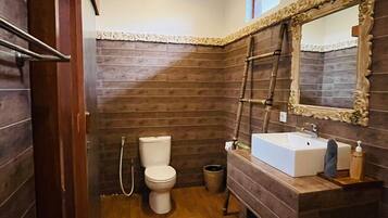 A compact bathroom with a wooden floor, a white toilet, a sink with a mirror, and a small trash bin.