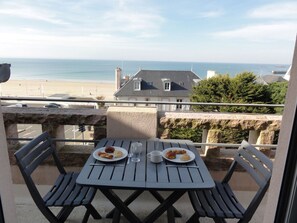 A balcony with a table set for two, overlooking a beach and the sea.