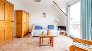 Un dormitorio con cama, armario de madera, una mesita, televisor y ventana con cortinas.