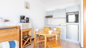 Una cocina compacta con una mesa y sillas de madera, un microondas, una cafetera y un refrigerador.