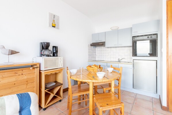 A compact kitchen with a wooden table and chairs, a microwave, a coffee maker, and a refrigerator.