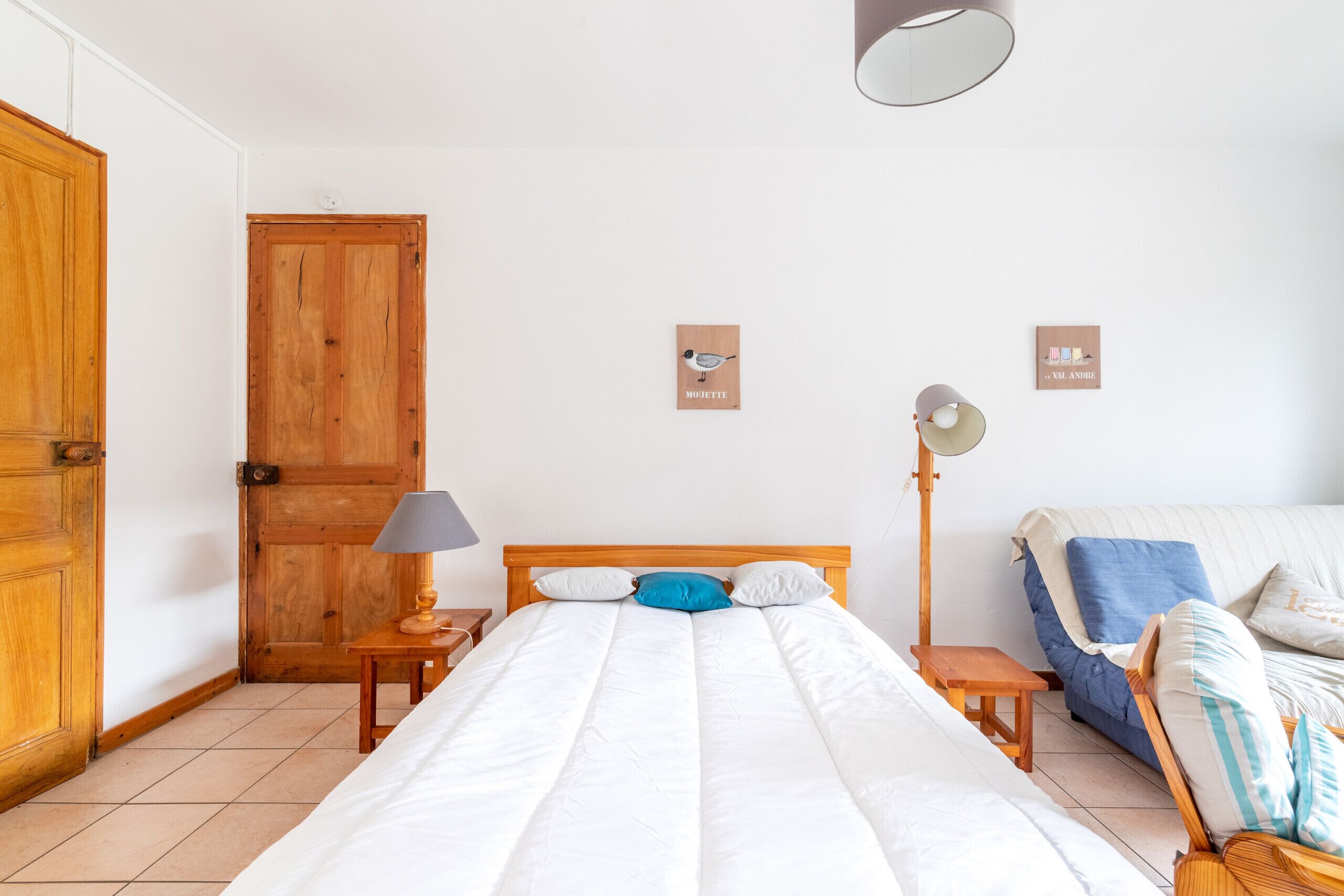 Une chambre à coucher avec un lit en bois, une table de chevet avec une lampe, une armoire en bois et une étagère murale agrémentée d’objets décoratifs.