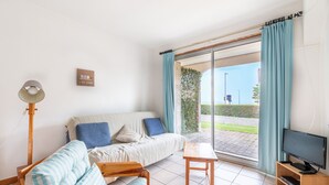 Un salon avec un canapé, une petite table, un téléviseur posé sur un meuble en bois et une lampe sur pied.