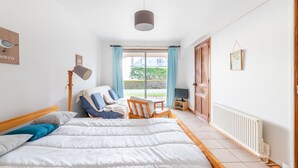 Une chambre à coucher avec un grand lit, une chaise, un bureau, une lampe et une fenêtre avec des rideaux.