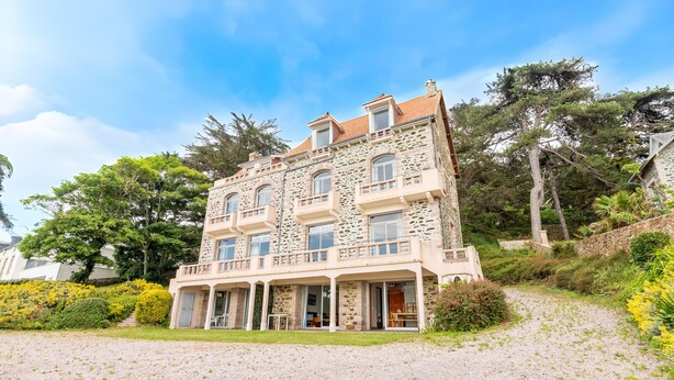 A multi-story stone building with balconies, a covered porch, and a gravel driveway. - Garden level with sea view in the heart of Pléneuf (Pléneuf-Val-André)
