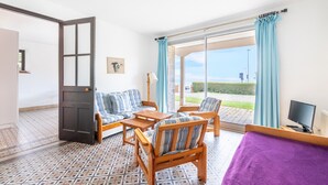 A room with a sofa, chairs, a small table, a bed, a TV, and a large window with curtains. - Garden level with sea view in the heart of Pléneuf (Pléneuf-Val-André)