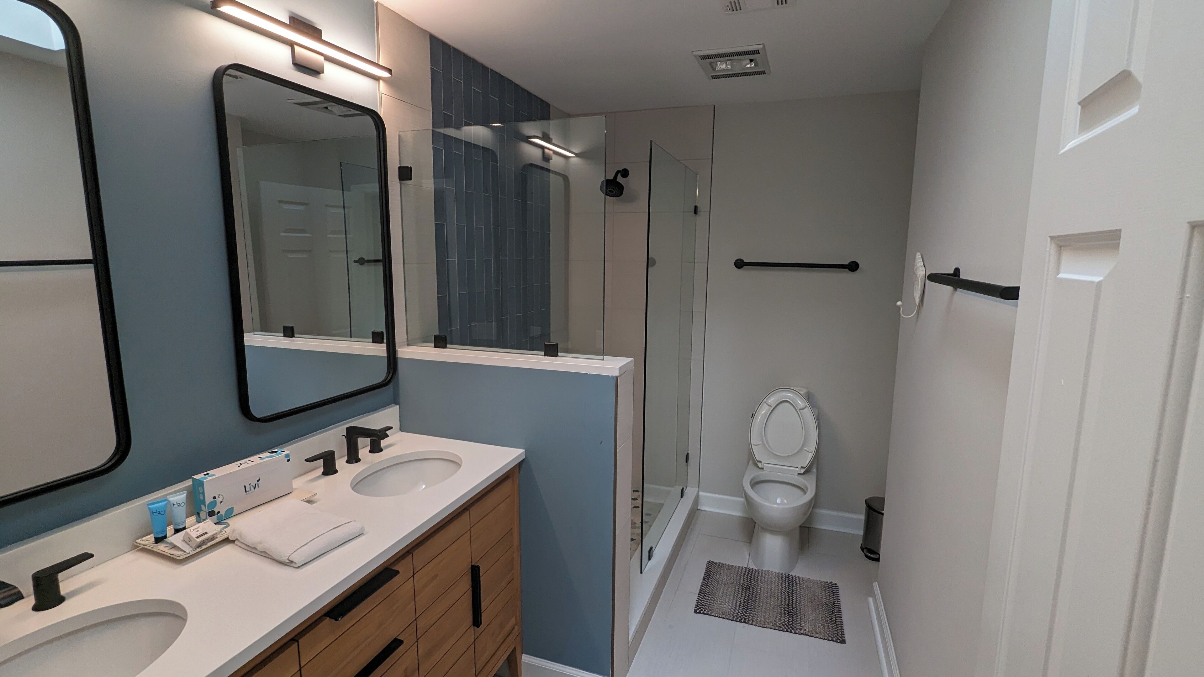Een moderne badkamer met een grote spiegel, twee wasbakken, een toilet en een douchecabine met glazen wanden.