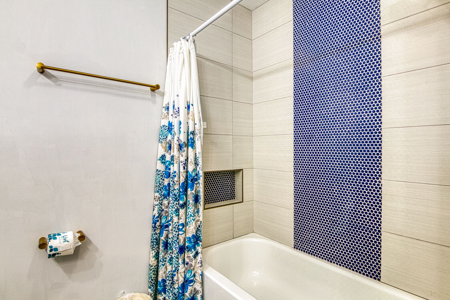A bathroom with a bathtub, a shower curtain with a floral pattern, and a towel rack.