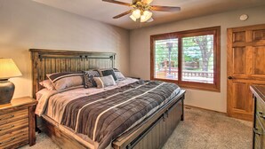 Een slaapkamer met een bed, houten hoofdeinde, een plafondventilator, een raam met zonwering en een deur.
