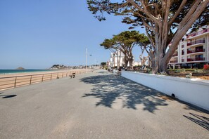 A coastal promenade with a beach, trees, and a white building with balconies. - Beachfront sea-view aprt,private parking, sleeps 4 (Pléneuf-Val-André)