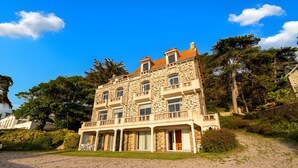 A multi-story stone building with a balcony, surrounded by trees and a gravel driveway. - 50m from the beach, charming flat with sea view (Pléneuf-Val-André)