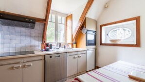 A compact kitchen with a dishwasher, oven, and a window with a view of a village. - 50m from the beach, charming flat with sea view (Pléneuf-Val-André)