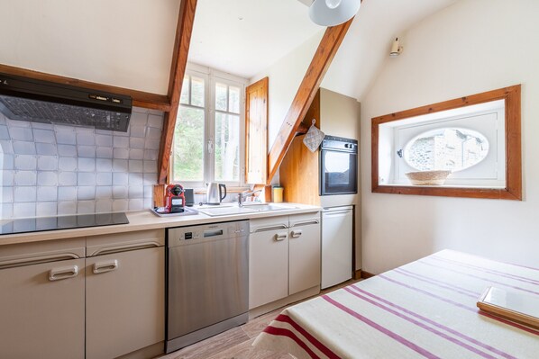 A compact kitchen with a dishwasher, oven, and a window with a view of a village.