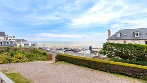 A coastal view with a parking area, a building with a balcony, and a beach in the background.