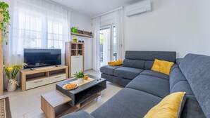 Een moderne woonkamer met een grijze bank, een flatscreen televisie, een houten entertainmentkast en een klein bijzettafeltje.