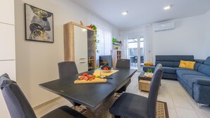 Een moderne woonkamer met een eethoek, met een donkere eettafel, zwarte stoelen, een blauwe bank en een grote spiegel.