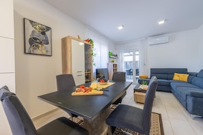 Una sala de estar moderna con comedor, que presenta un comedor de madera oscura, sillas negras, un sofá azul y un espejo grande.