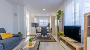 Een moderne woonkamer met een bank, salontafel, televisie en een eethoek.