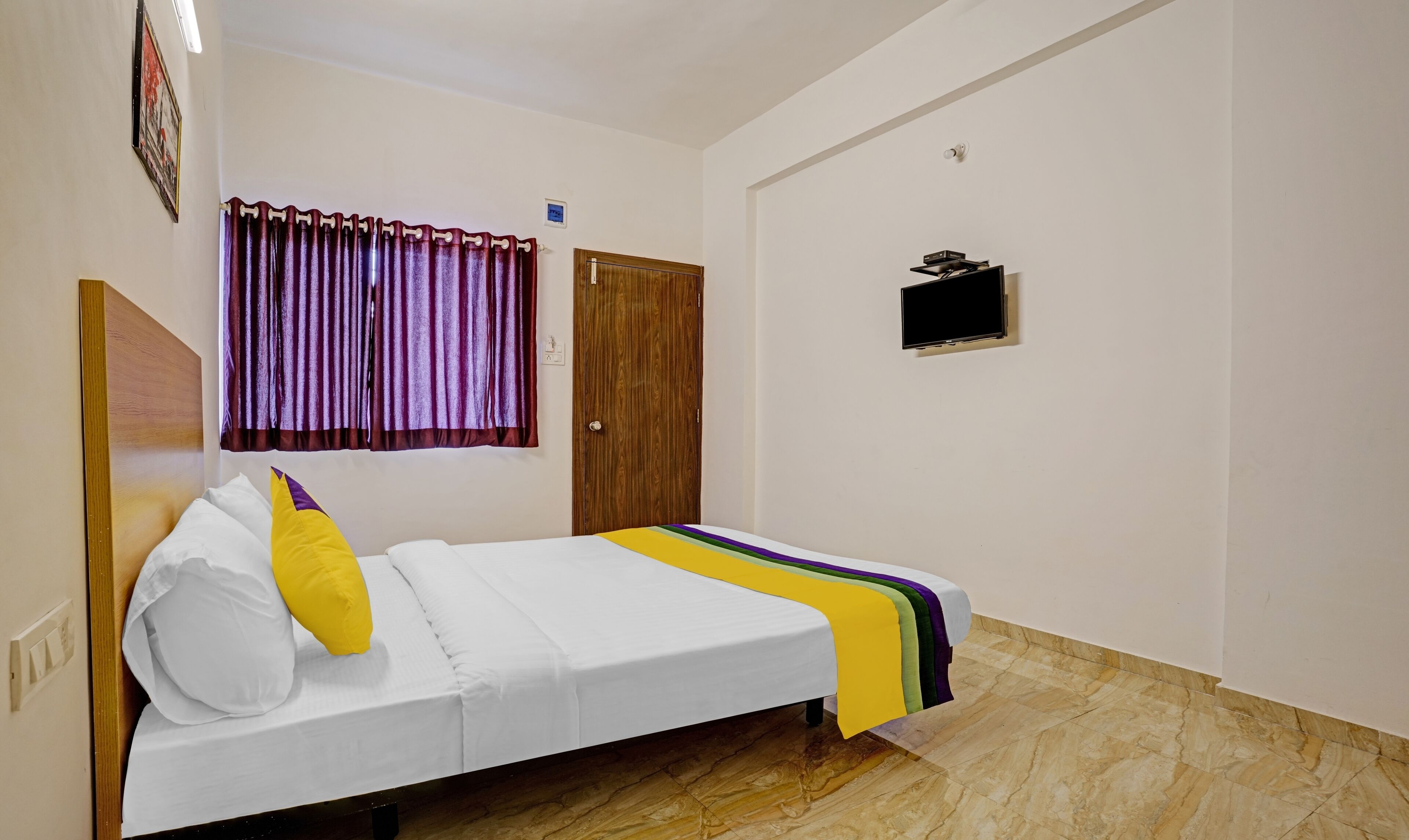 Un dormitorio con cama, una puerta de madera, un televisor pequeño y una cortina.