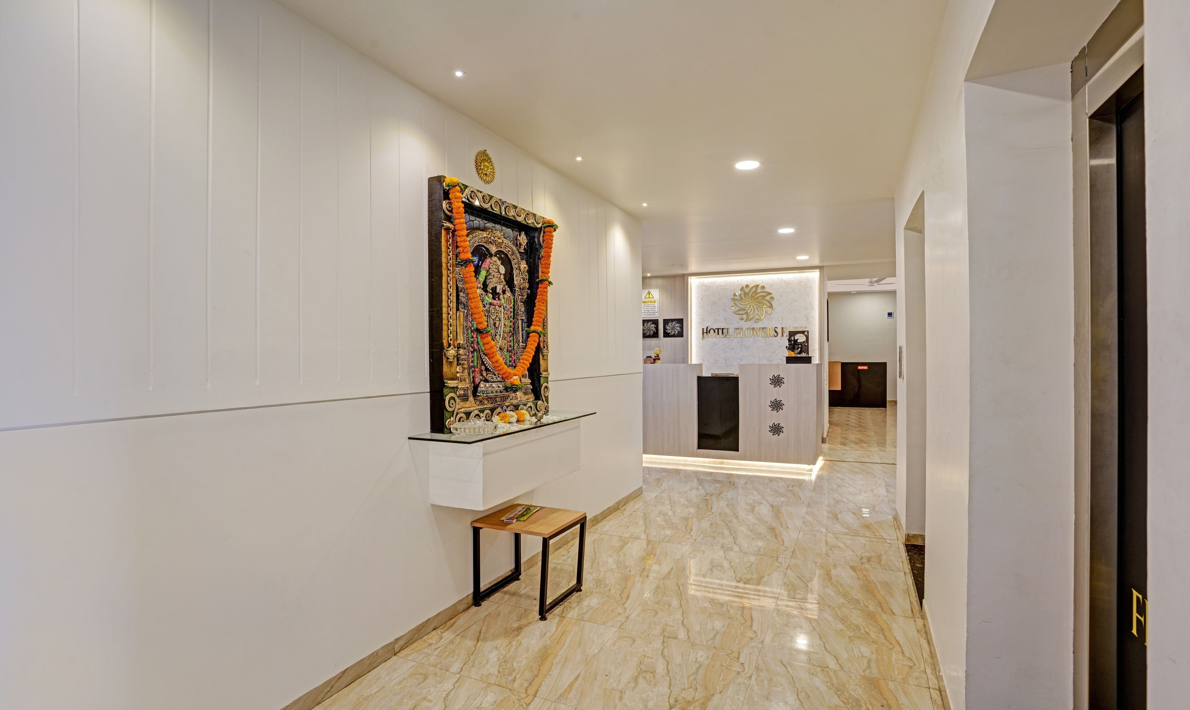 A hotel reception area with a marble floor, a reception desk, and a decorative statue on the wall.