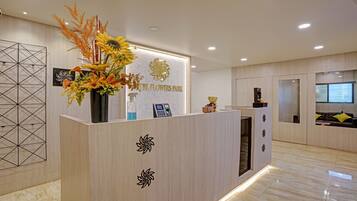 A reception desk with a sign reading "El Flowers Park," a vase with flowers, a teddy bear, and a small statue.