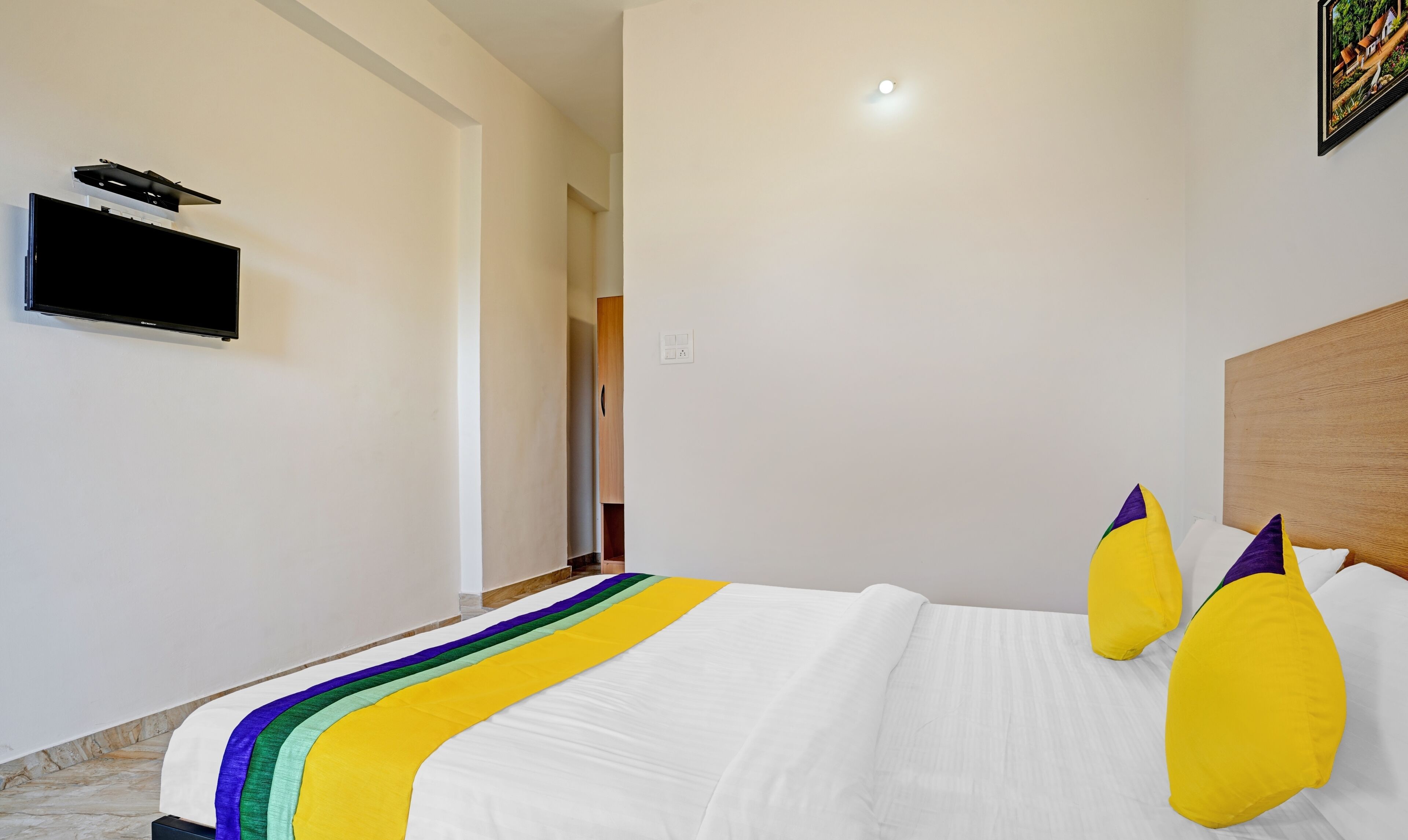 A hotel room with a large bed, a flat-screen TV mounted on the wall, and a wooden headboard.