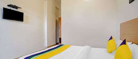 A hotel room with a large bed, a flat-screen TV mounted on the wall, and a wooden headboard.