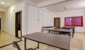 Une salle de conférence dotée d’un sol en marbre, de murs blancs et d’une porte en bois. Des tables et des chaises y sont disposées pour les réunions.