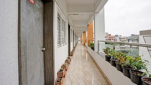 A corridor with wooden doors, potted plants, and a view of buildings in the distance. - Itsy Hotels Flowers Park (Nashik)