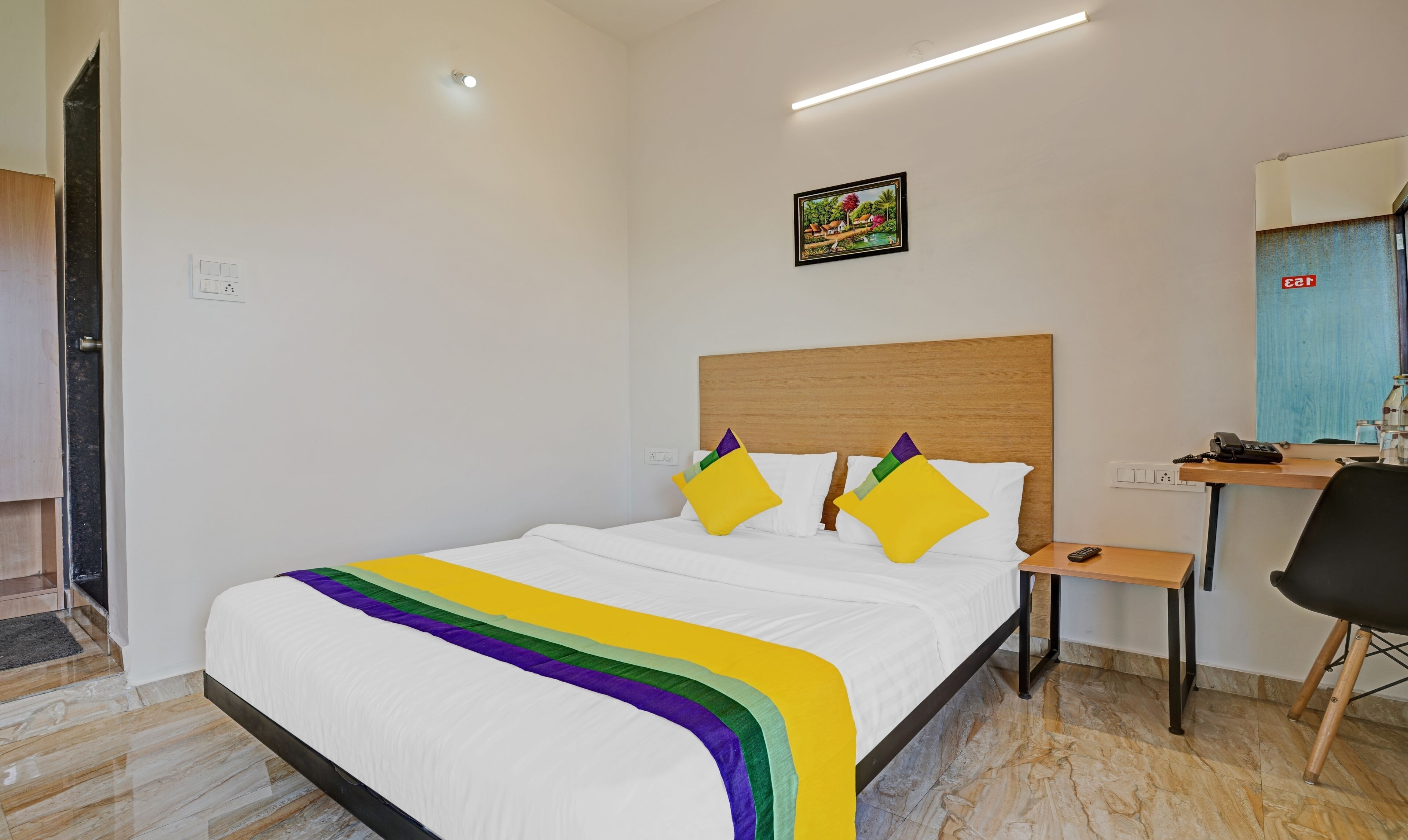 A hotel room with a bed, bedside table, and a desk with a chair.