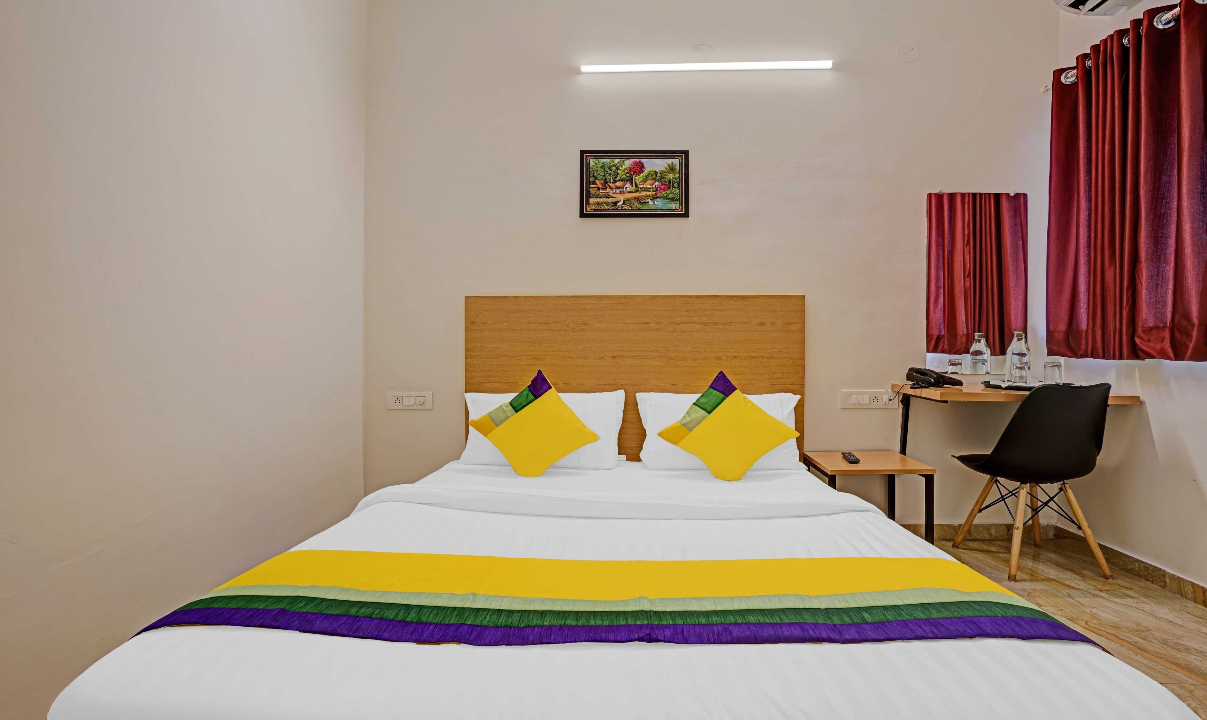 Una habitación de hotel con cama, escritorio, silla y un cuadro en la pared.